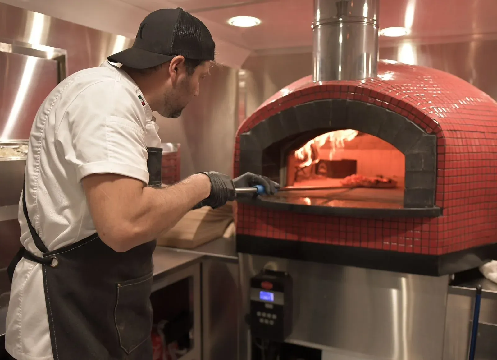 Chef sliding a pizza into the red wood-fired oven