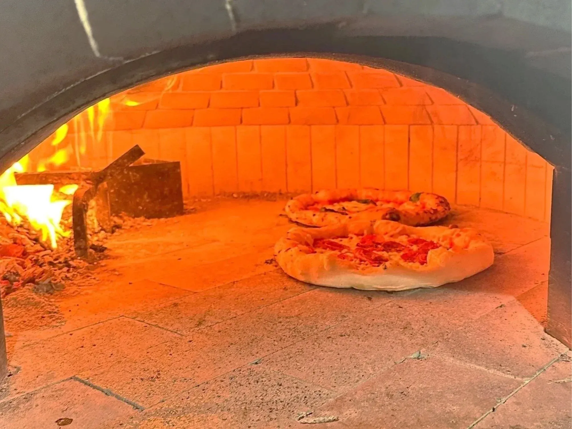 Two pizzas baking on the stone floor of the wood-fired oven